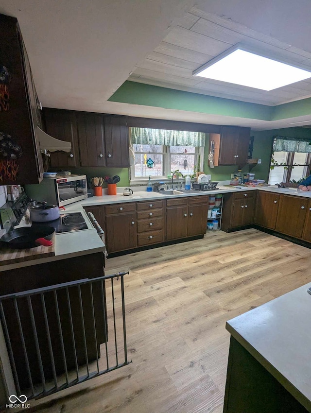 kitchen with light countertops, a tray ceiling, stainless steel microwave, and light wood finished floors