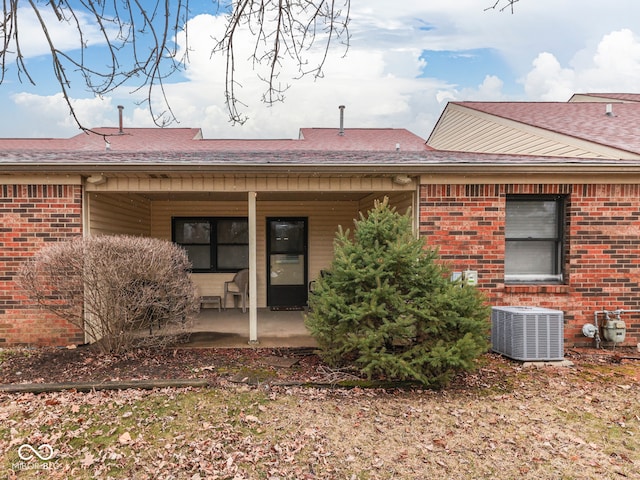 rear view of house with a patio, brick siding, central AC, and roof with shingles