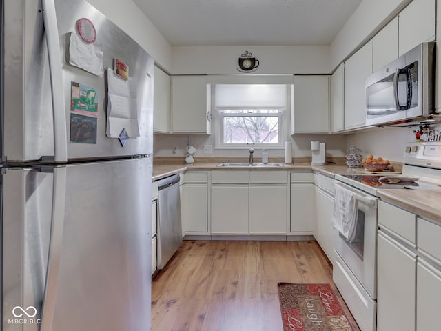 kitchen featuring a sink, white cabinetry, appliances with stainless steel finishes, light wood finished floors, and light countertops