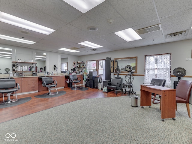 carpeted home office with visible vents, a paneled ceiling, and wood finished floors