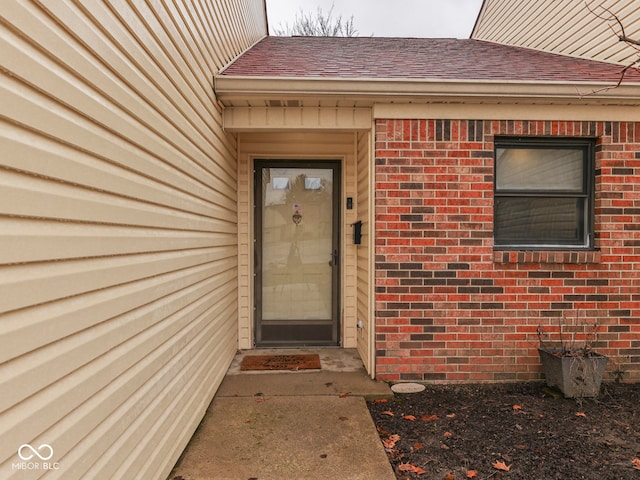 entrance to property with brick siding and a shingled roof