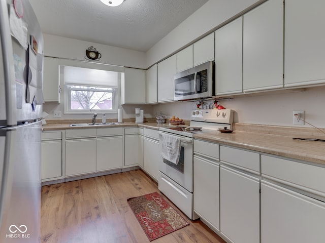 kitchen with white cabinetry, stainless steel appliances, light countertops, and a sink