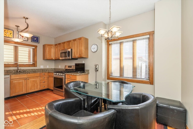 kitchen featuring dark stone counters, light tile patterned flooring, appliances with stainless steel finishes, decorative light fixtures, and a notable chandelier