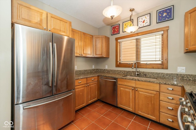 kitchen with a sink, dark tile patterned floors, stone countertops, and stainless steel appliances