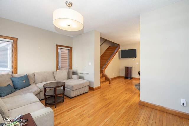 living area with stairs, baseboards, and light wood-type flooring