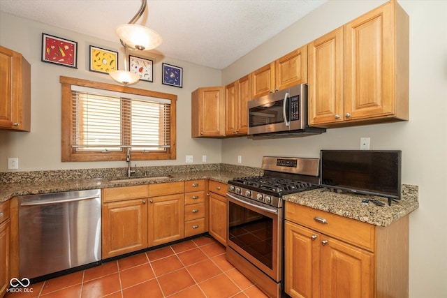 kitchen with tile patterned flooring, stone counters, stainless steel appliances, a textured ceiling, and a sink