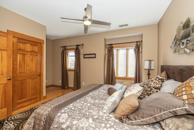 bedroom with a ceiling fan, wood finished floors, visible vents, and baseboards