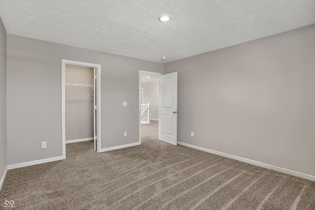 unfurnished bedroom featuring a textured ceiling, a spacious closet, recessed lighting, carpet floors, and baseboards