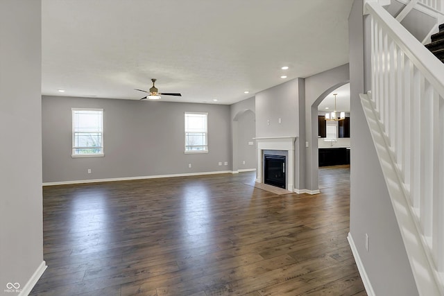 unfurnished living room featuring baseboards, recessed lighting, dark wood finished floors, arched walkways, and ceiling fan