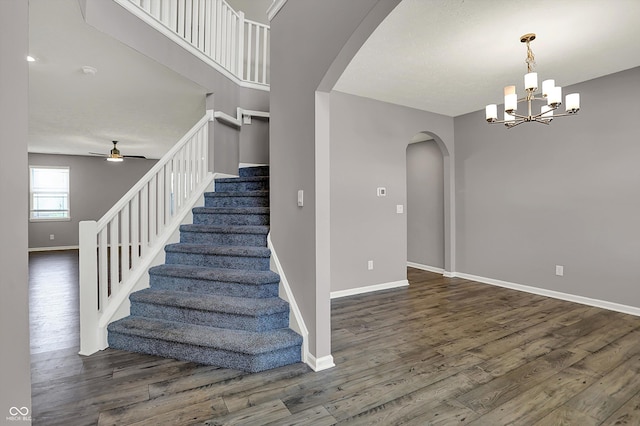 stairs featuring baseboards, arched walkways, wood finished floors, and ceiling fan with notable chandelier