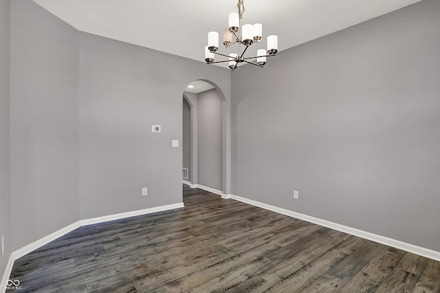 unfurnished room with arched walkways, baseboards, an inviting chandelier, and dark wood finished floors
