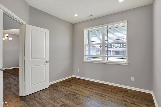 spare room featuring visible vents, baseboards, a chandelier, and wood finished floors