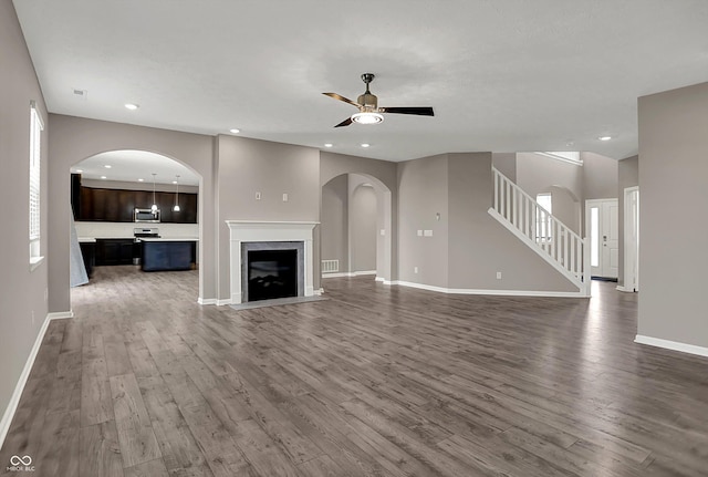 unfurnished living room with a ceiling fan, baseboards, dark wood-style floors, and stairs