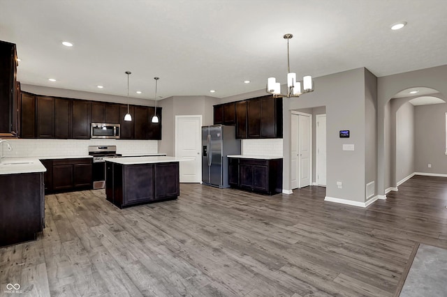 kitchen with dark brown cabinetry, arched walkways, a sink, stainless steel appliances, and decorative backsplash