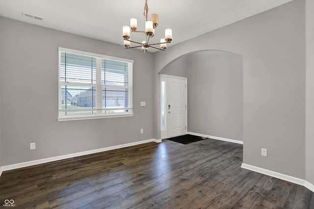 interior space with a chandelier, arched walkways, dark wood-type flooring, and baseboards