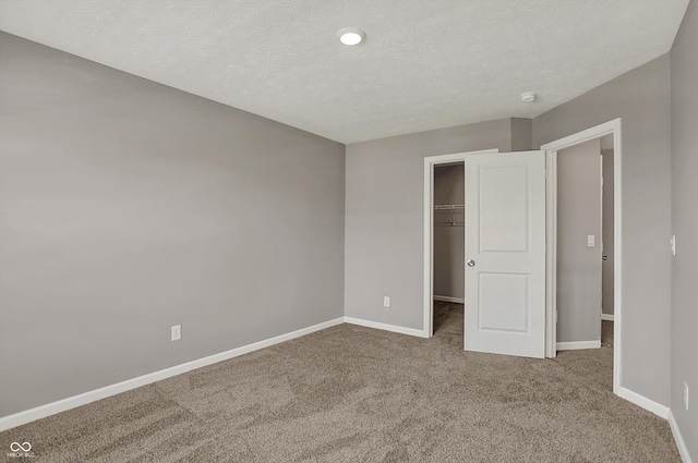 unfurnished bedroom with a spacious closet, baseboards, a textured ceiling, and carpet floors