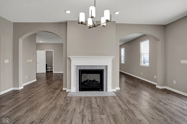 unfurnished living room with a fireplace, baseboards, an inviting chandelier, and wood finished floors