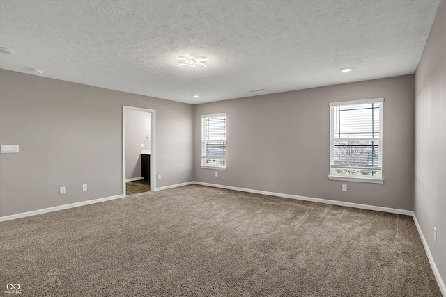 unfurnished room featuring a textured ceiling, a healthy amount of sunlight, baseboards, and carpet