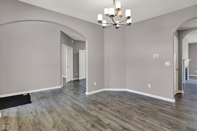 unfurnished room with arched walkways, wood finished floors, an inviting chandelier, and baseboards