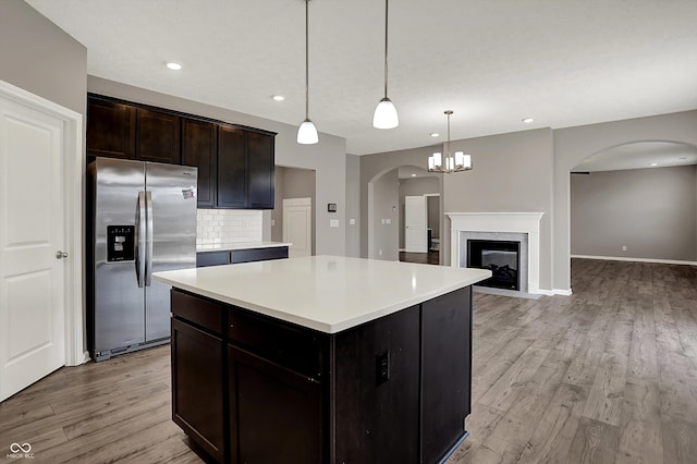 kitchen featuring tasteful backsplash, arched walkways, stainless steel fridge, light countertops, and light wood finished floors