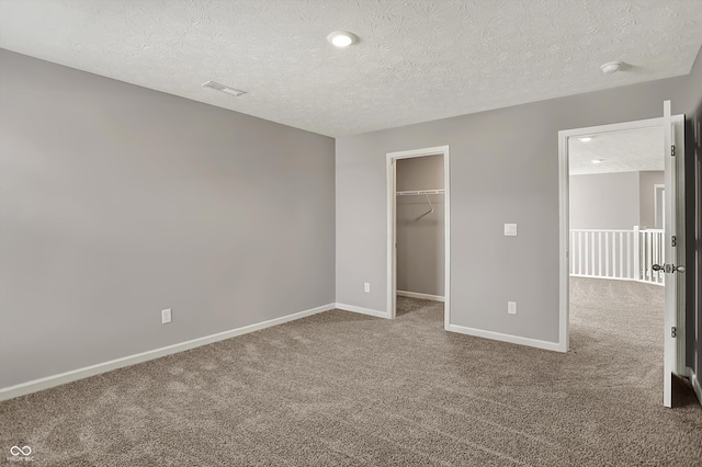 unfurnished bedroom with a spacious closet, carpet flooring, a textured ceiling, and baseboards