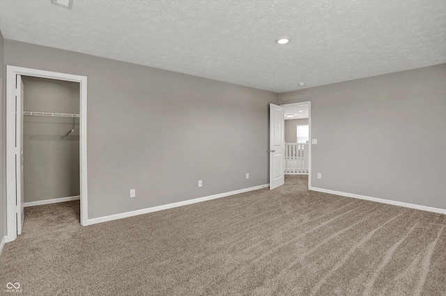 unfurnished bedroom with baseboards, a walk in closet, carpet, and a textured ceiling