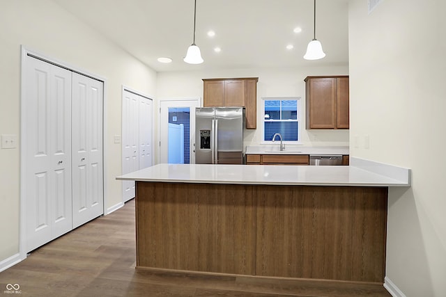 kitchen featuring a peninsula, dark wood-style flooring, a sink, appliances with stainless steel finishes, and decorative light fixtures