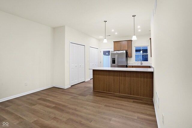 kitchen with stainless steel fridge, a peninsula, dark wood-type flooring, and a sink