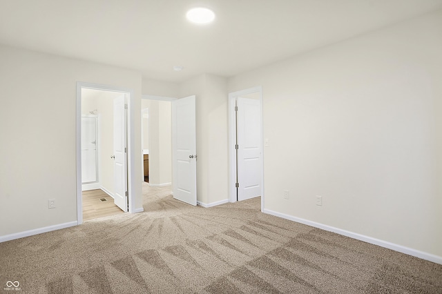 unfurnished bedroom with light carpet, ensuite bathroom, and baseboards