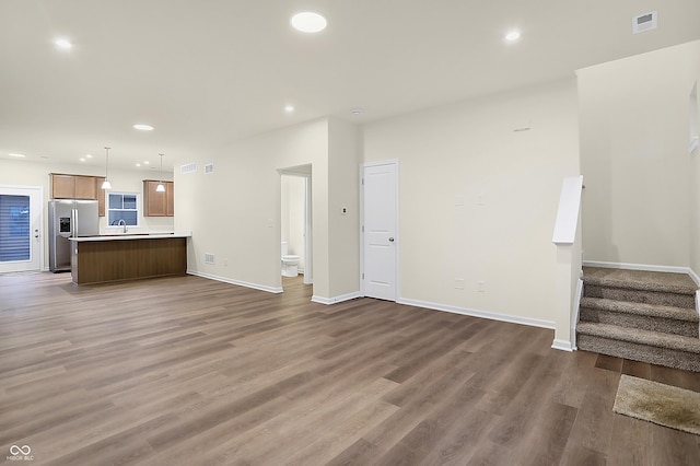 unfurnished living room with a sink, recessed lighting, wood finished floors, and stairs