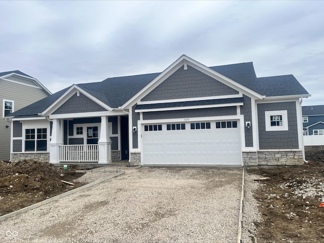 craftsman-style house with roof with shingles, covered porch, a garage, stone siding, and driveway