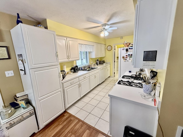 kitchen with white appliances, a ceiling fan, light countertops, a textured ceiling, and a sink