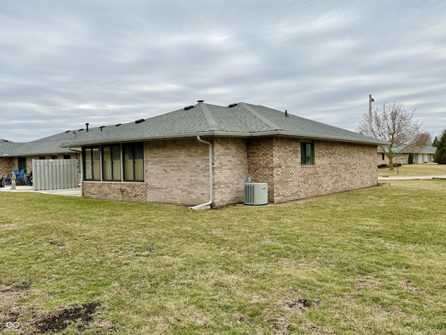 view of side of property featuring central AC, brick siding, a lawn, and roof with shingles