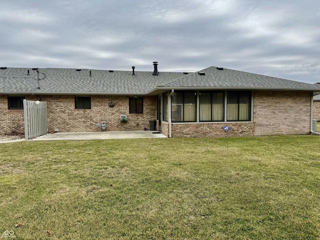 rear view of property with brick siding, roof with shingles, a patio area, and a lawn