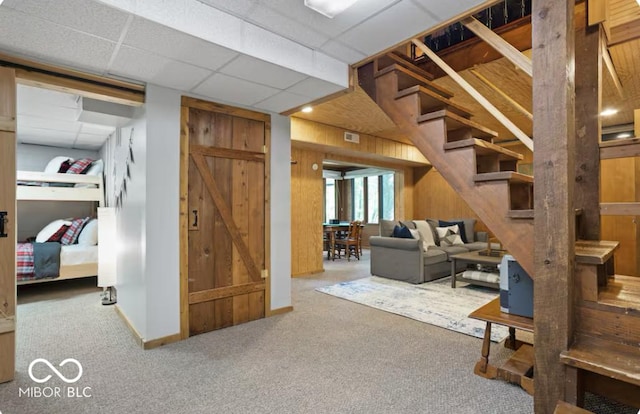 basement featuring visible vents, a drop ceiling, carpet, wooden walls, and stairs