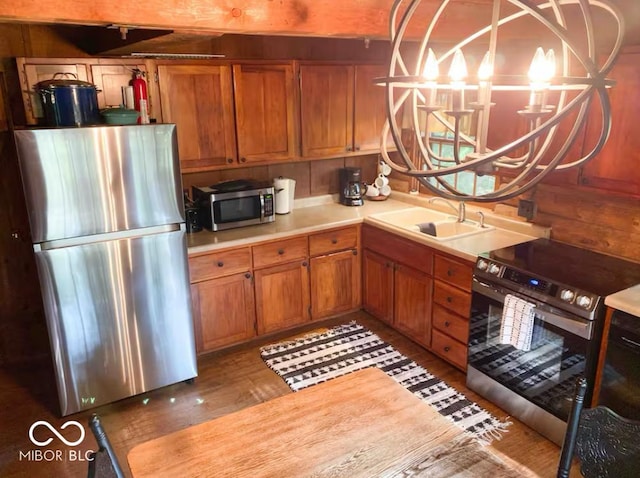 kitchen featuring a sink, wood finished floors, stainless steel appliances, brown cabinetry, and light countertops