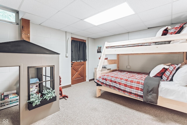 bedroom featuring carpet flooring, concrete block wall, and a paneled ceiling