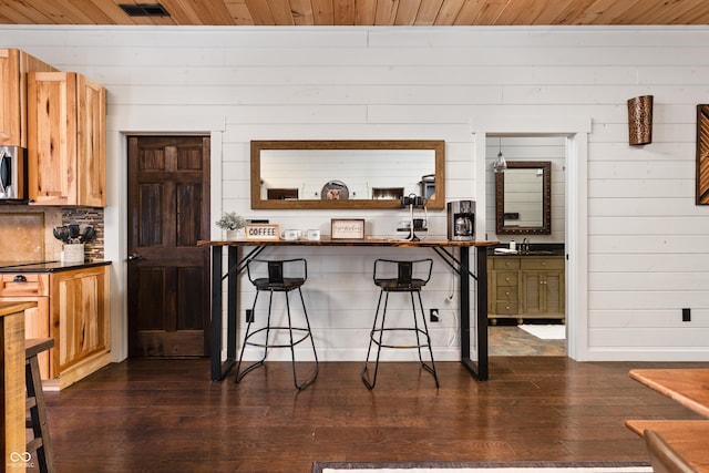 kitchen with a sink, stainless steel microwave, dark countertops, dark wood finished floors, and a breakfast bar area