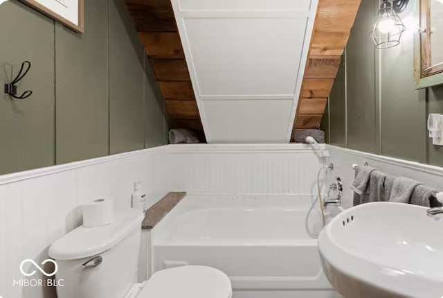 full bath with a decorative wall, toilet, a bath, and a sink