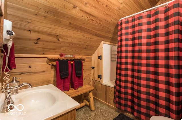 full bath with a sink, wooden walls, wooden ceiling, tile patterned flooring, and lofted ceiling