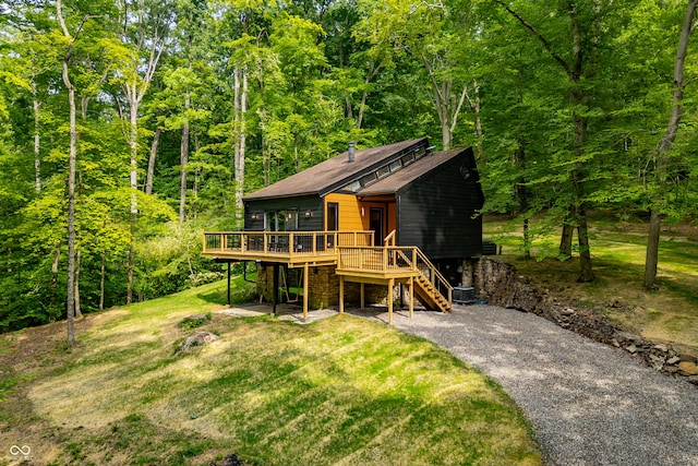 chalet / cabin featuring a deck, driveway, a front lawn, stairway, and a wooded view