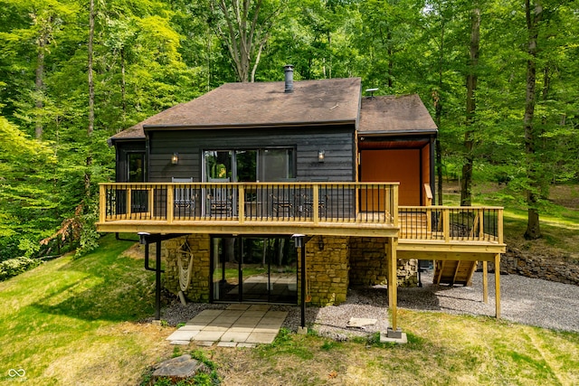 back of house featuring a view of trees, a yard, stone siding, a deck, and a patio area