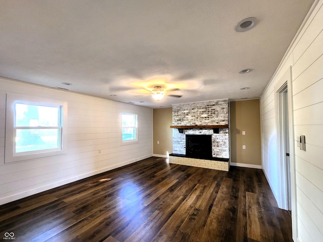 unfurnished living room with a brick fireplace, ceiling fan, baseboards, and dark wood finished floors