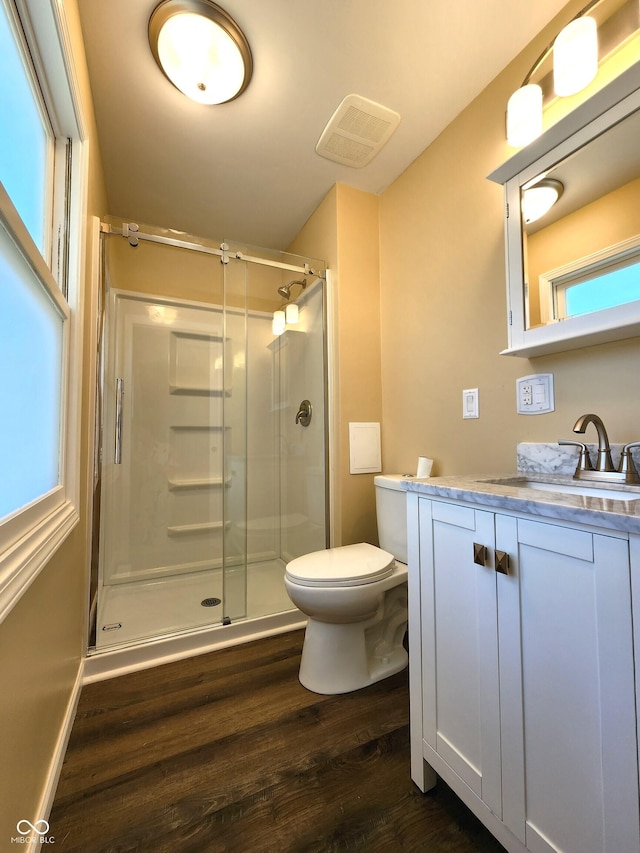 bathroom with visible vents, toilet, vanity, a shower stall, and wood finished floors