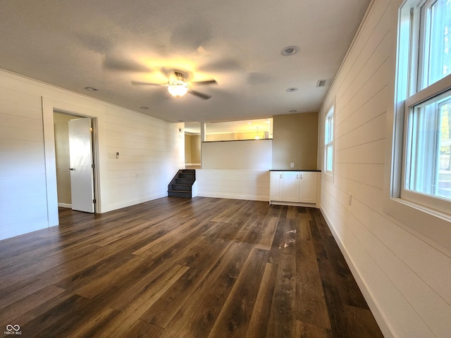 unfurnished living room with dark wood-style flooring, visible vents, and stairway