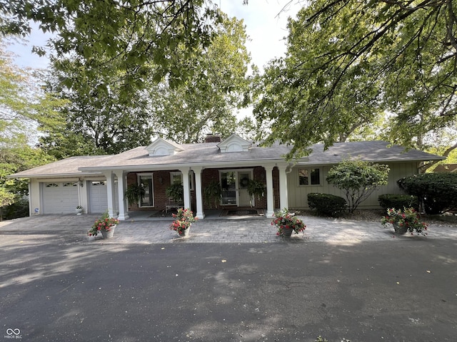 ranch-style home with a porch, an attached garage, brick siding, and driveway