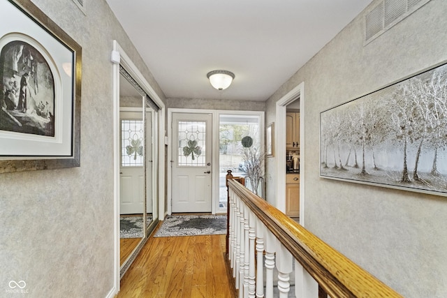 corridor featuring light wood-style flooring, an upstairs landing, and visible vents