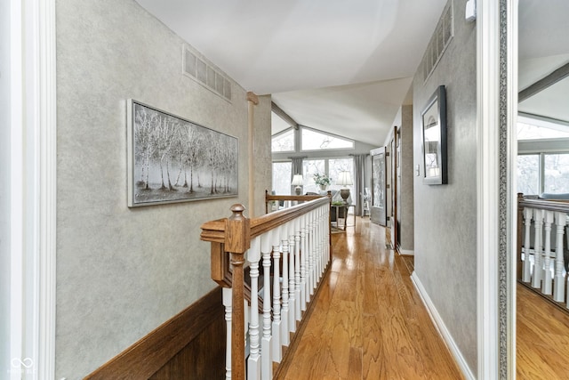 hallway with wood finished floors, an upstairs landing, visible vents, and lofted ceiling