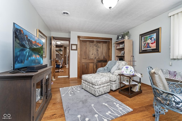 living area with baseboards, visible vents, light wood finished floors, and a textured ceiling