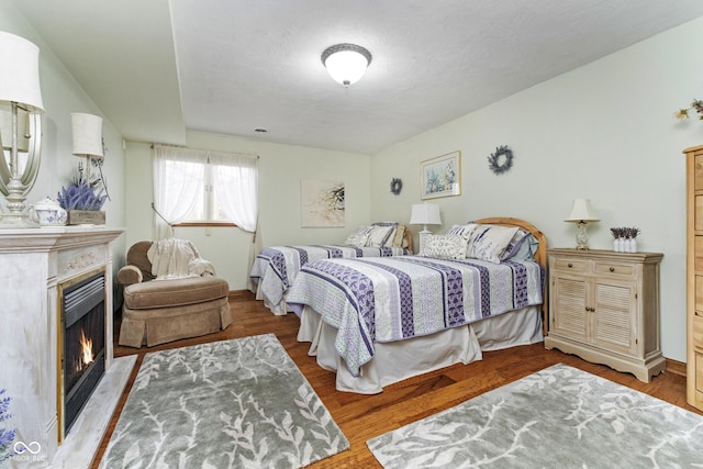 bedroom featuring wood finished floors and a warm lit fireplace